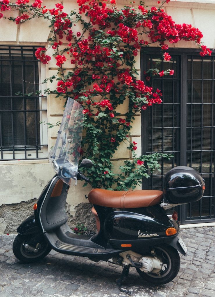 a scooter parked in front of a building with red flowers